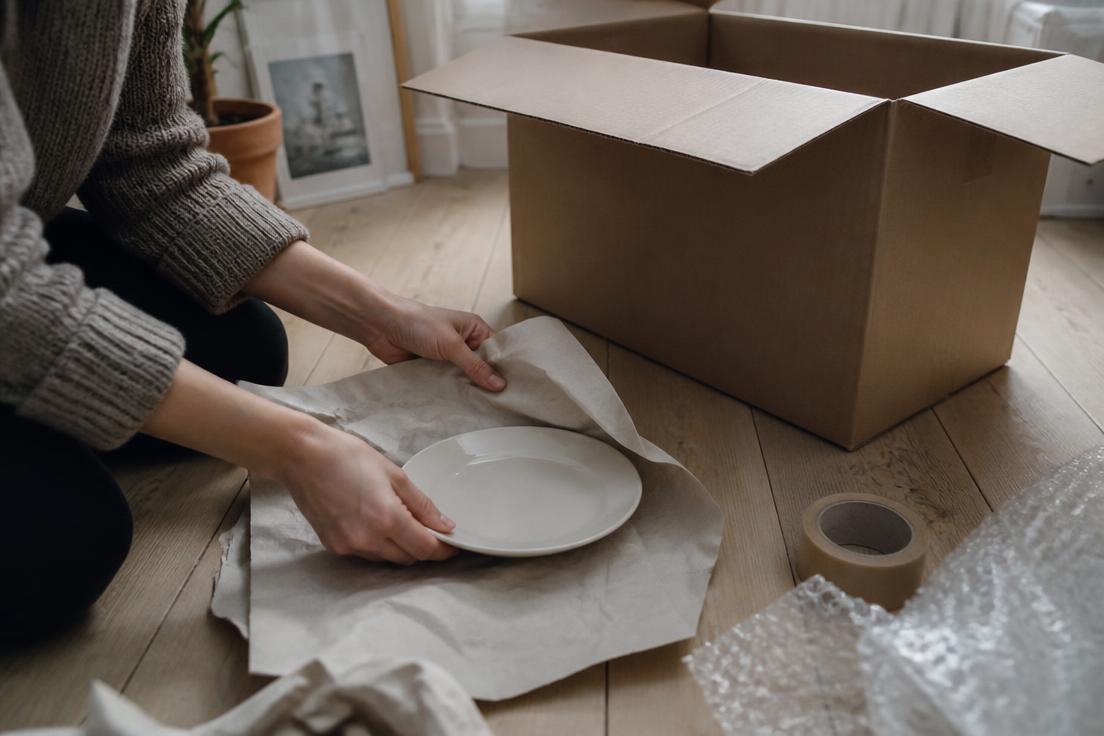 Person packar porslin i en flyttkartong med bubbelplast på köksbordet
